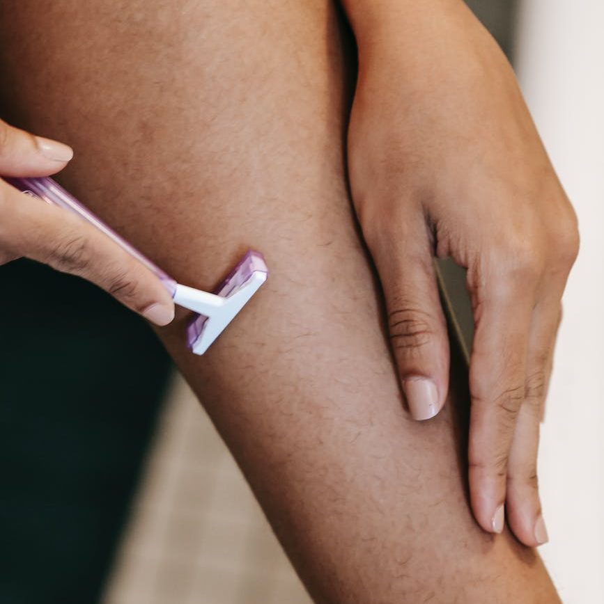 crop ethnic woman shaving leg with disposable razor